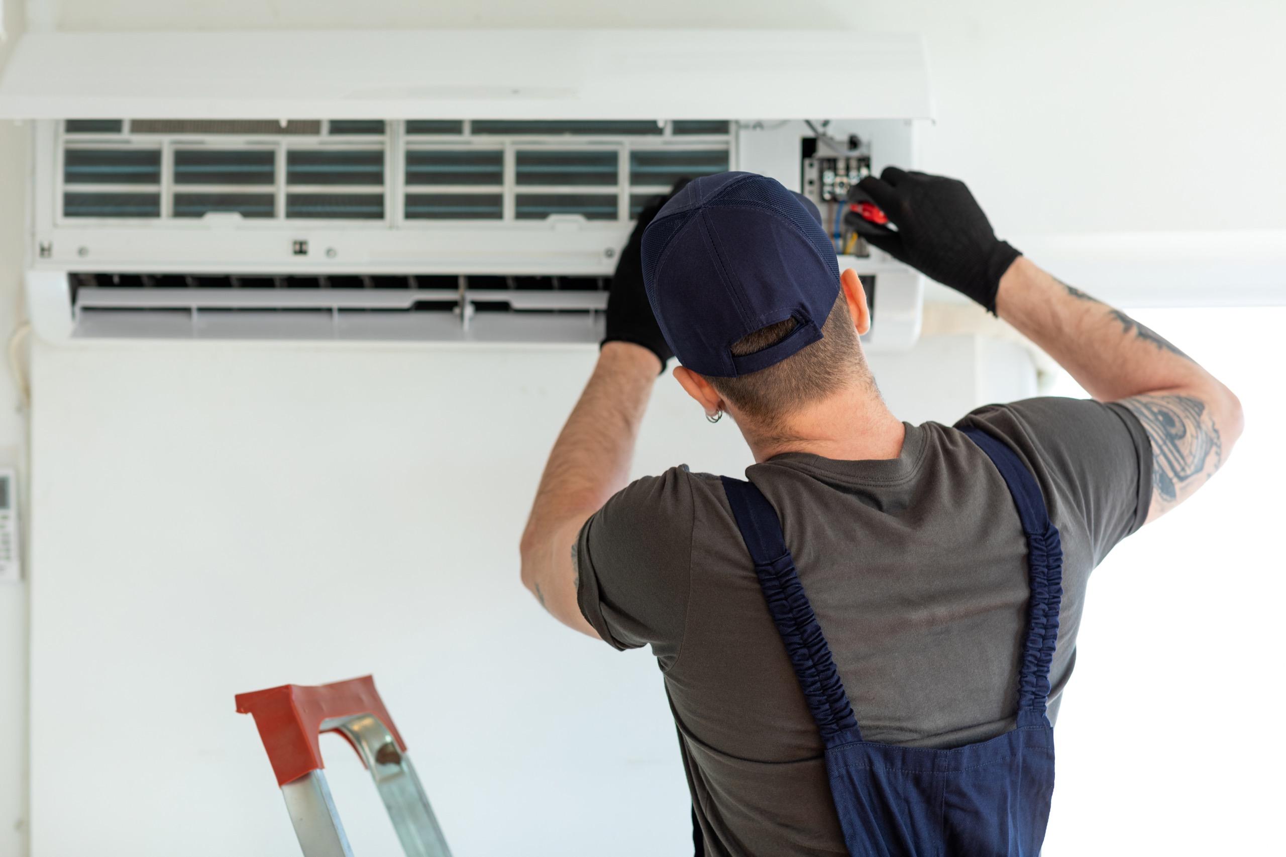 Male technician working on air conditioning unit with tools.