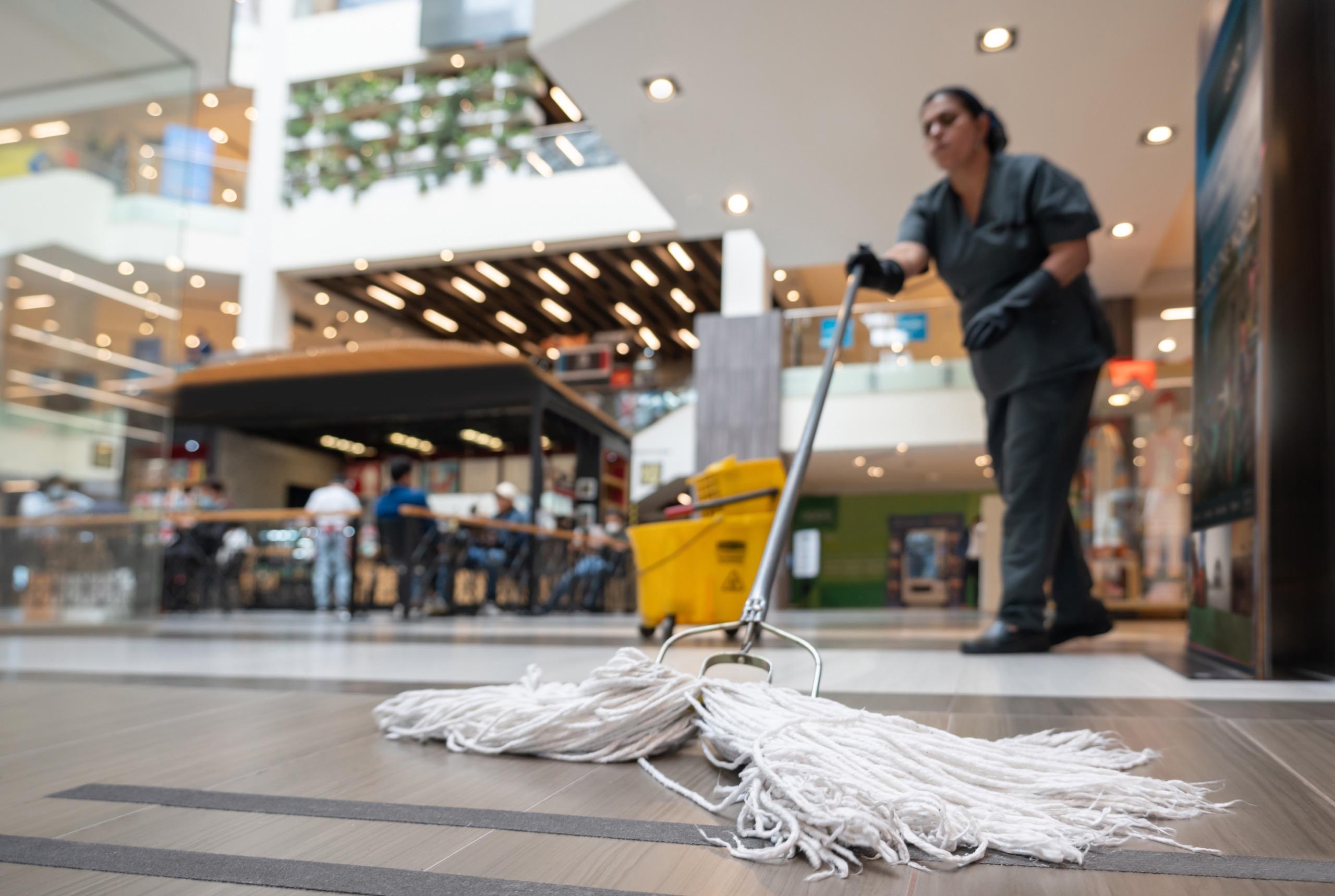 Cleaner mopping floor with bucket and mop inside a shopping center.