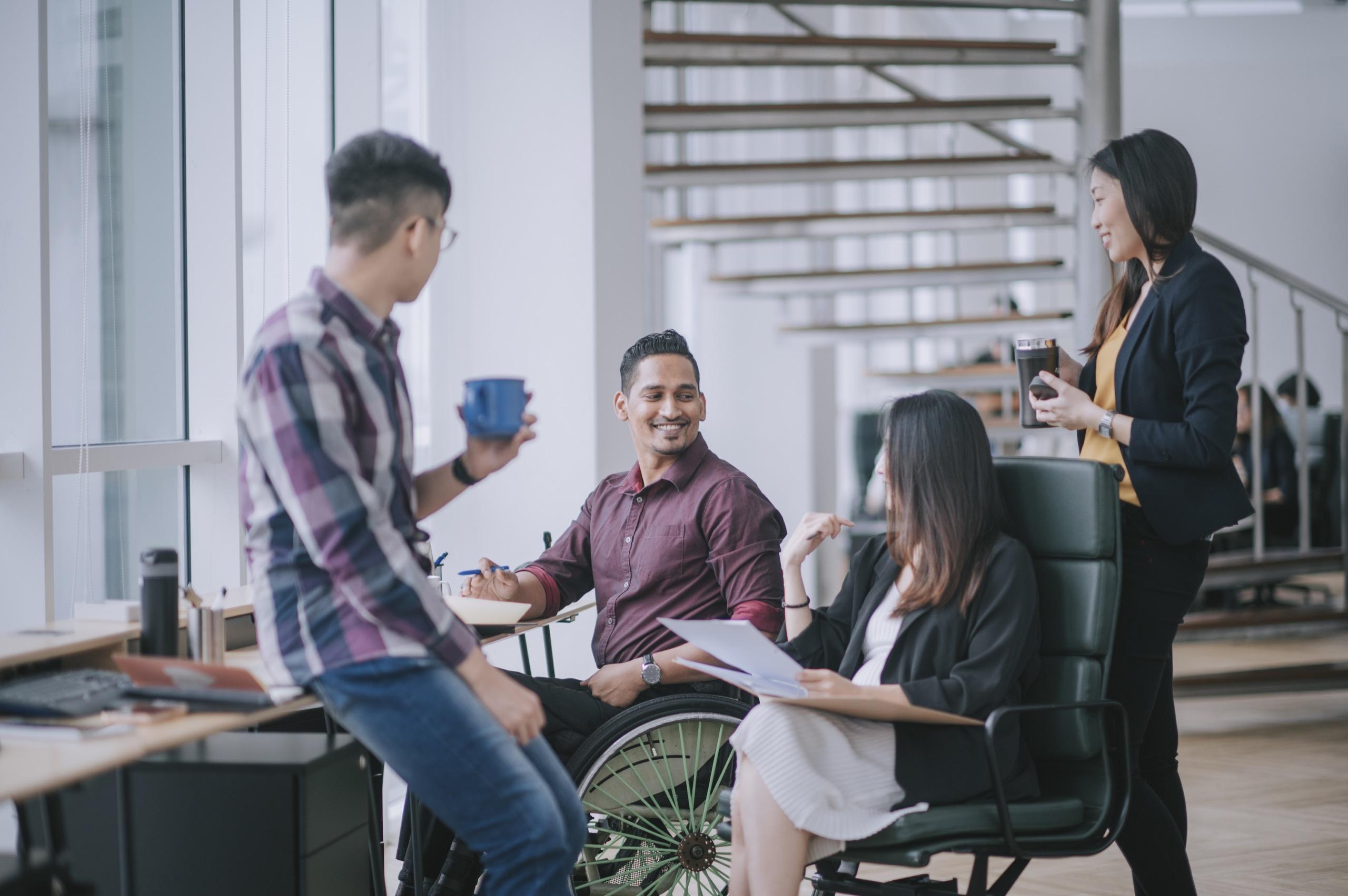 Group of diverse coworkers, including a person in a wheelchair, having an informal meeting in office.