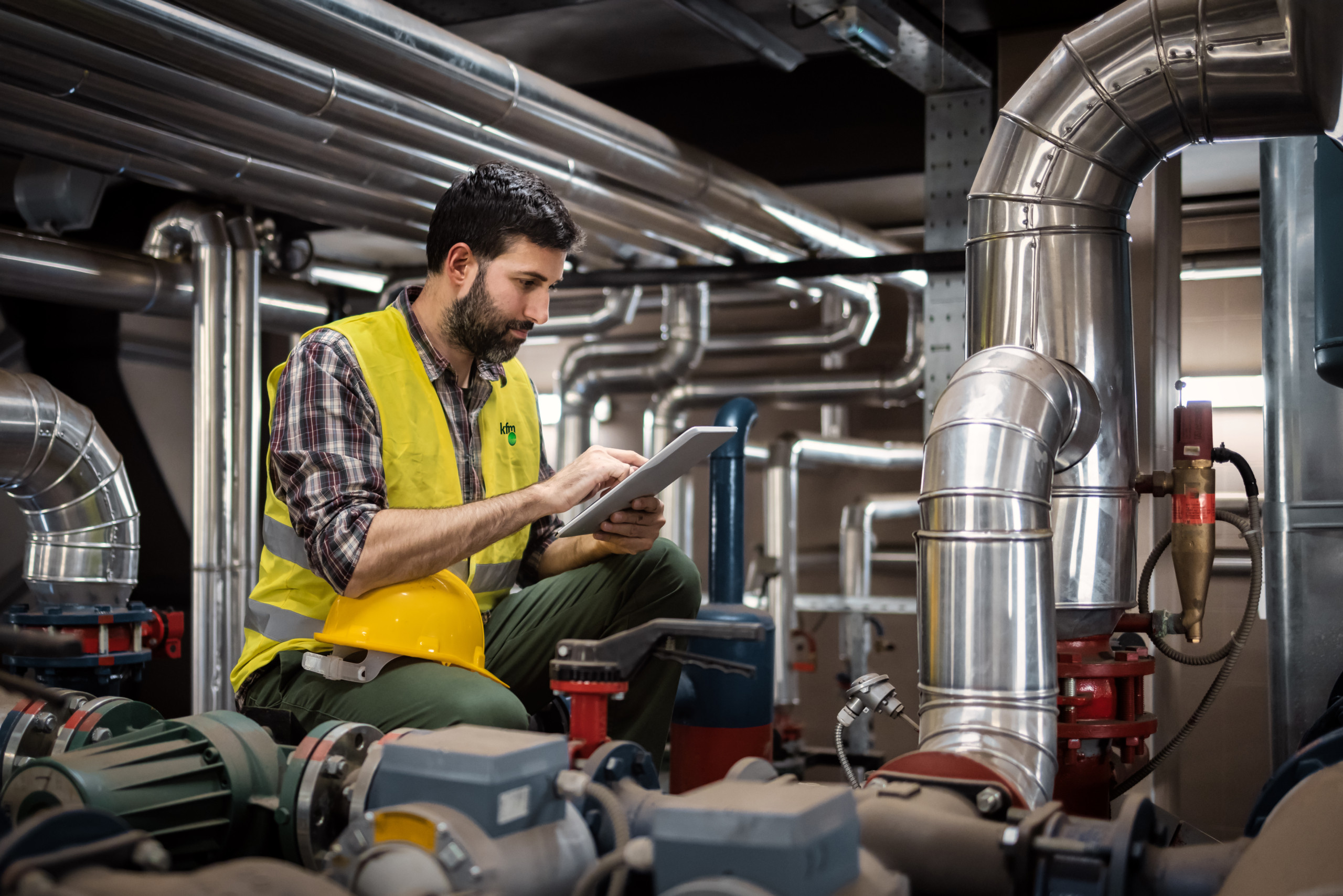 Engineer checking industrial plant equipment with tablet inside plant room.