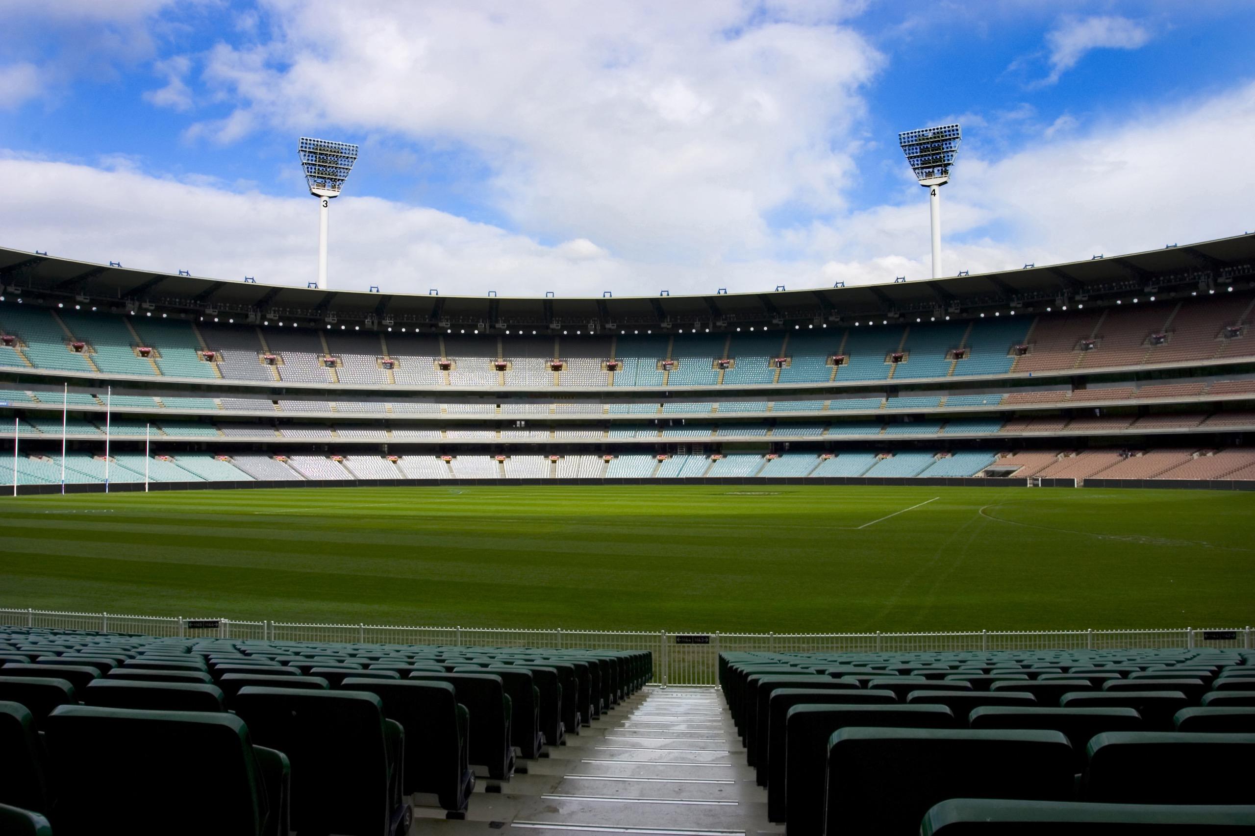 Empty stadium with green grass field and rows of seats under bright sky.