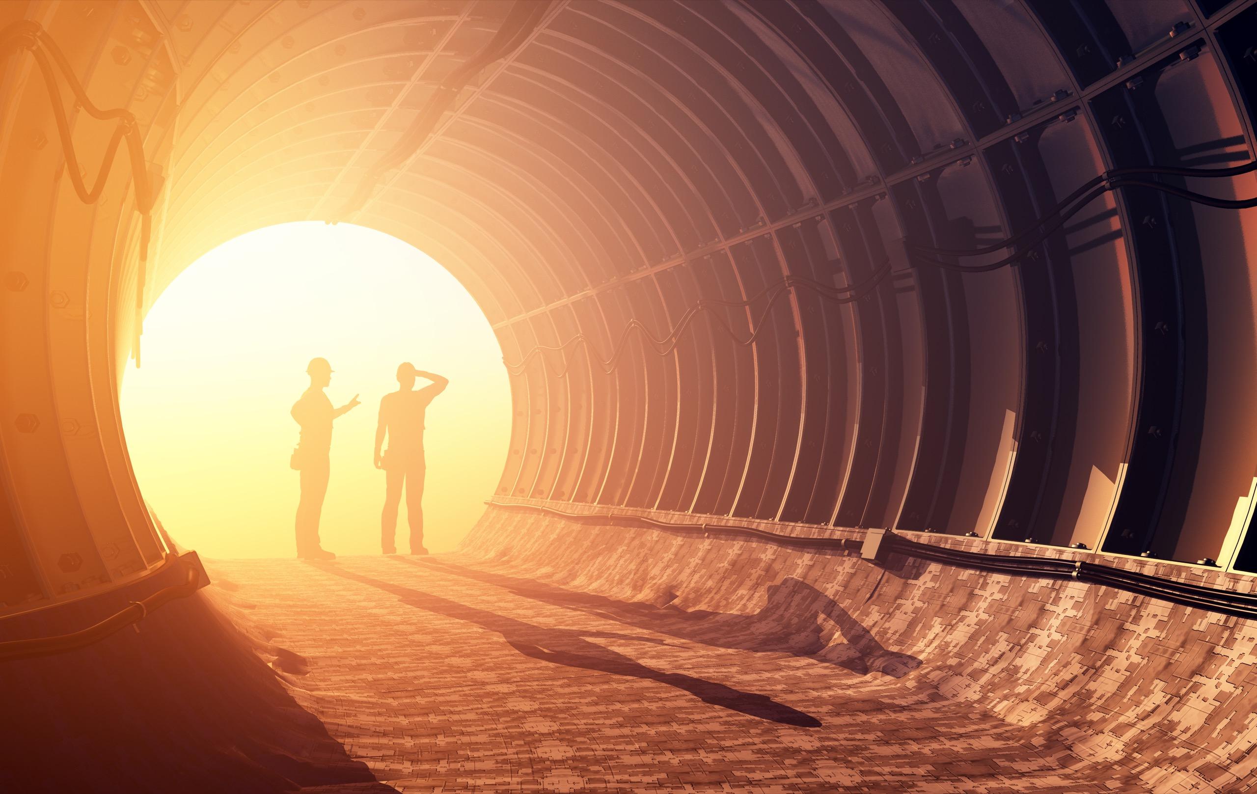 Silhouettes of two workers talking inside a tunnel with strong sunlight behind them.