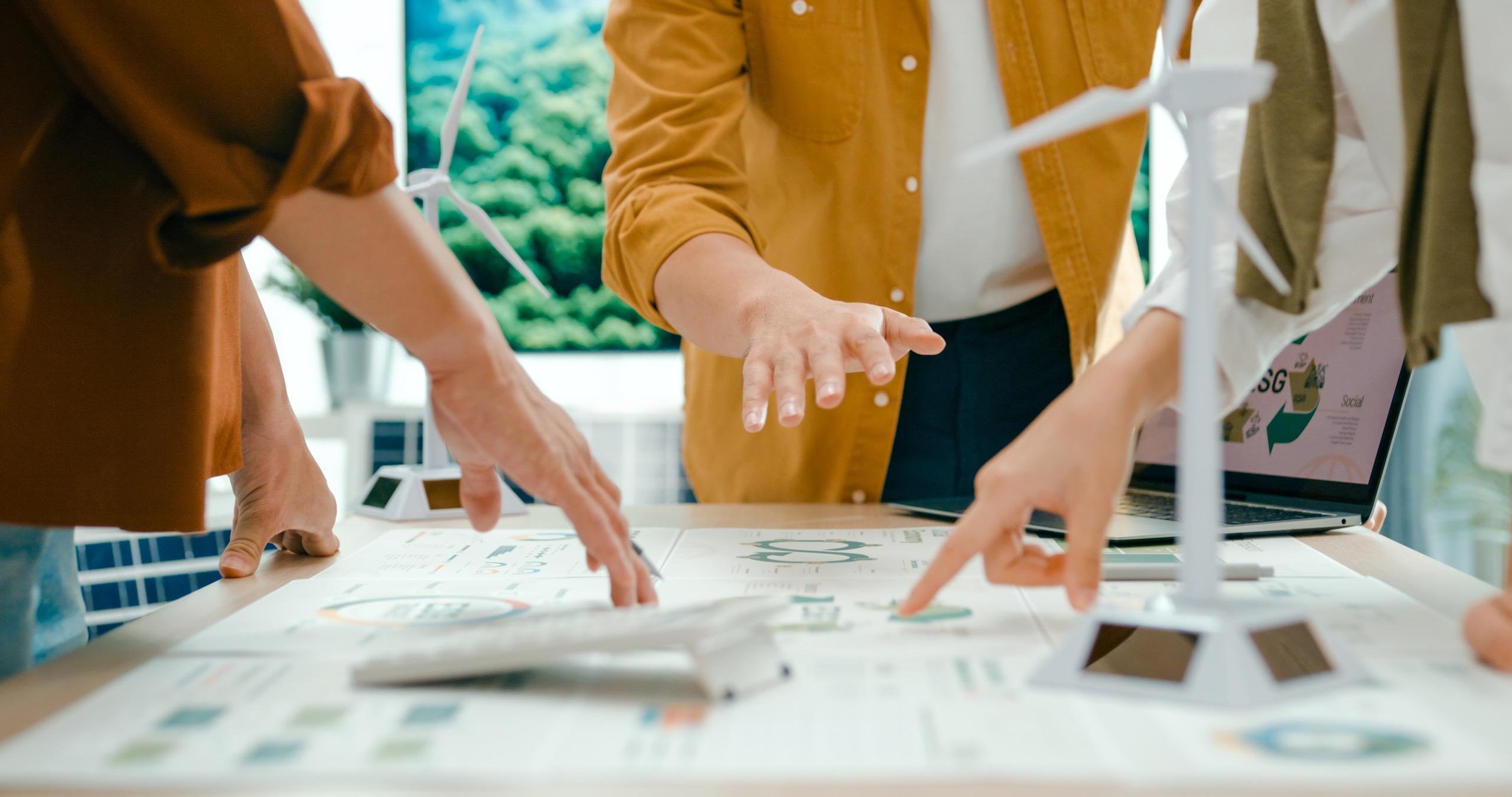 Team members pointing at renewable energy models and charts during a sustainability strategy meeting.