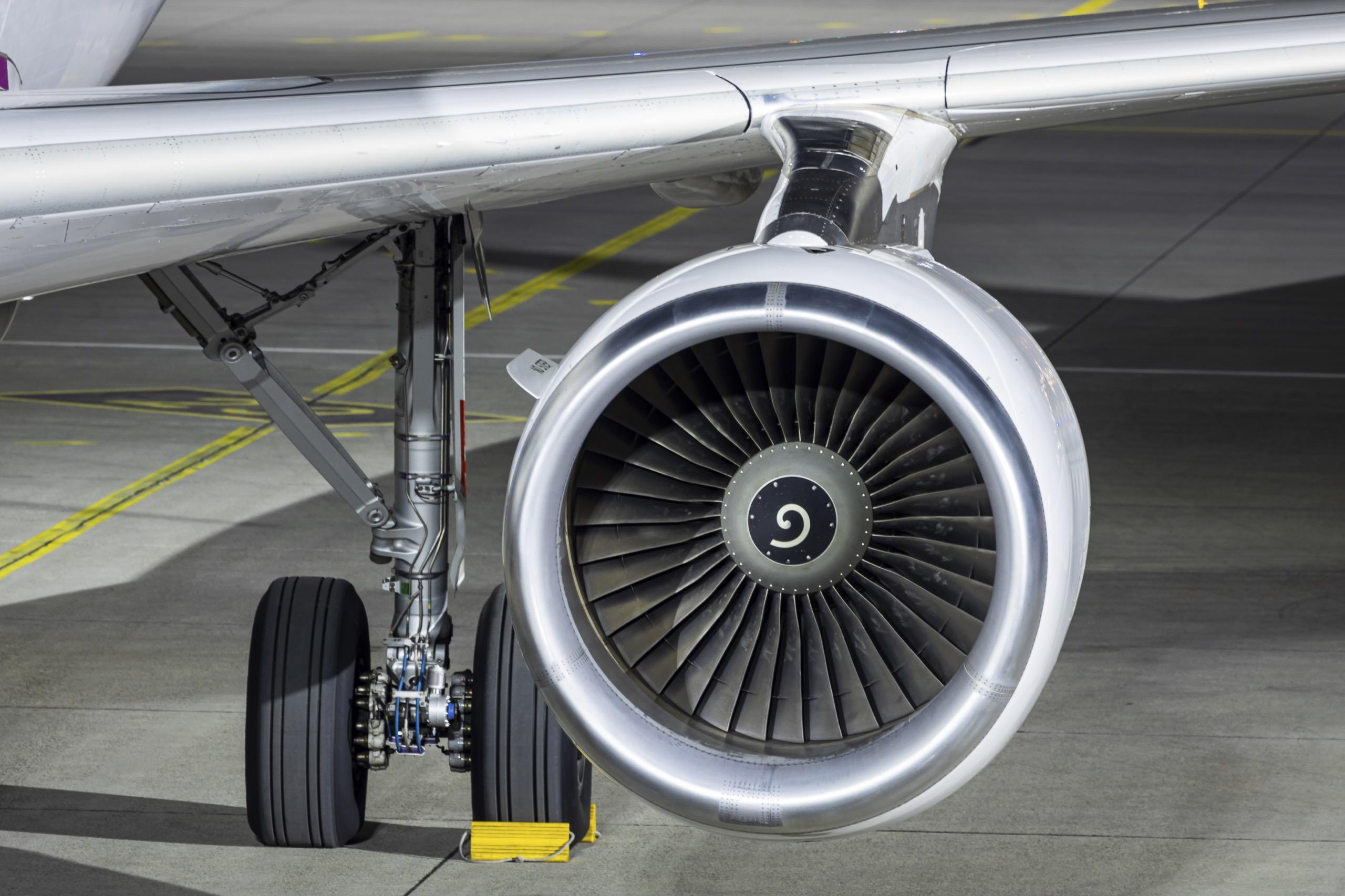 Close-up of a commercial jet engine turbine with landing gear visible on the tarmac.
