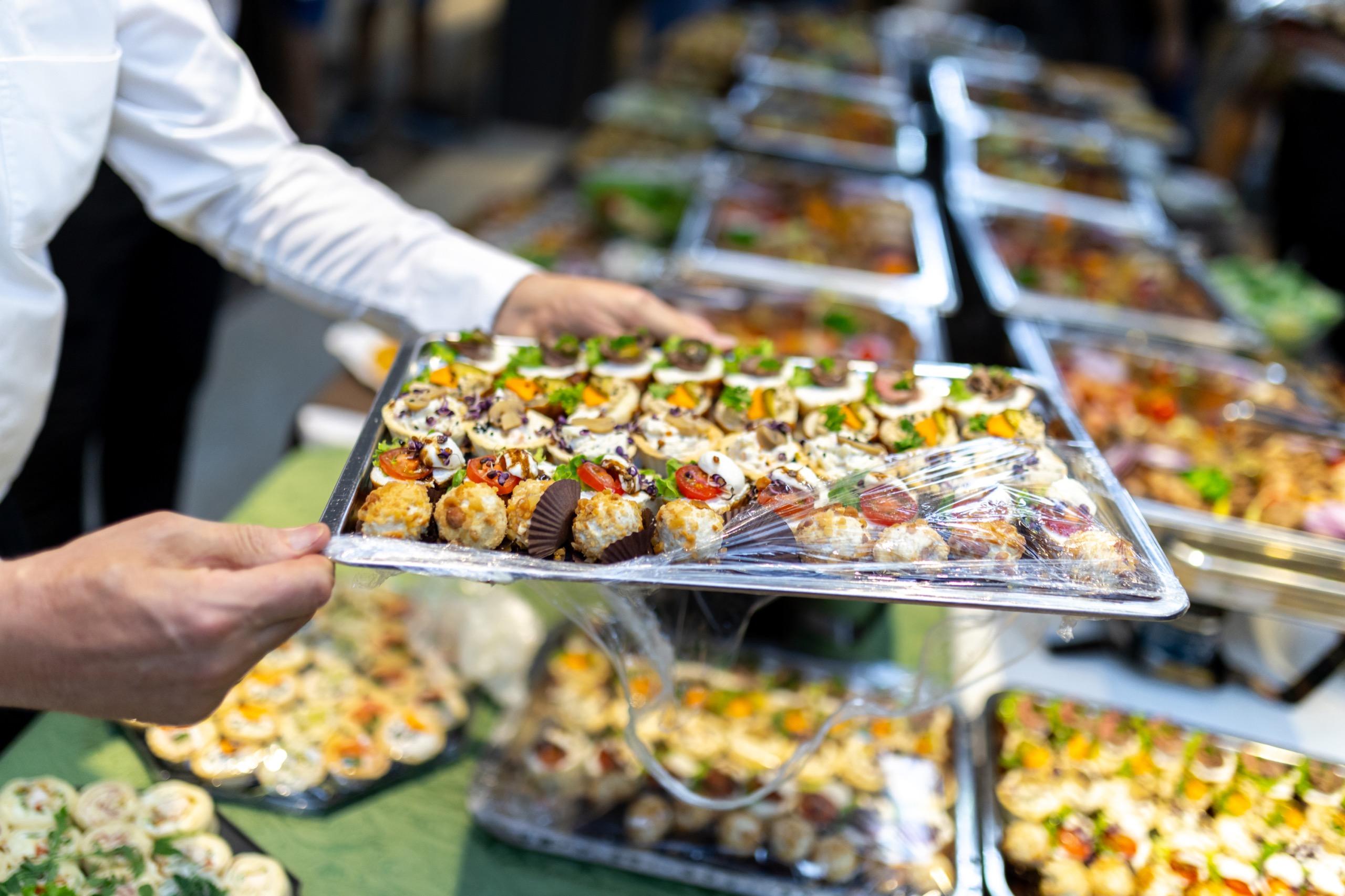 Catering staff member arranging a tray of assorted canapés and appetizers at a corporate event buffet table.