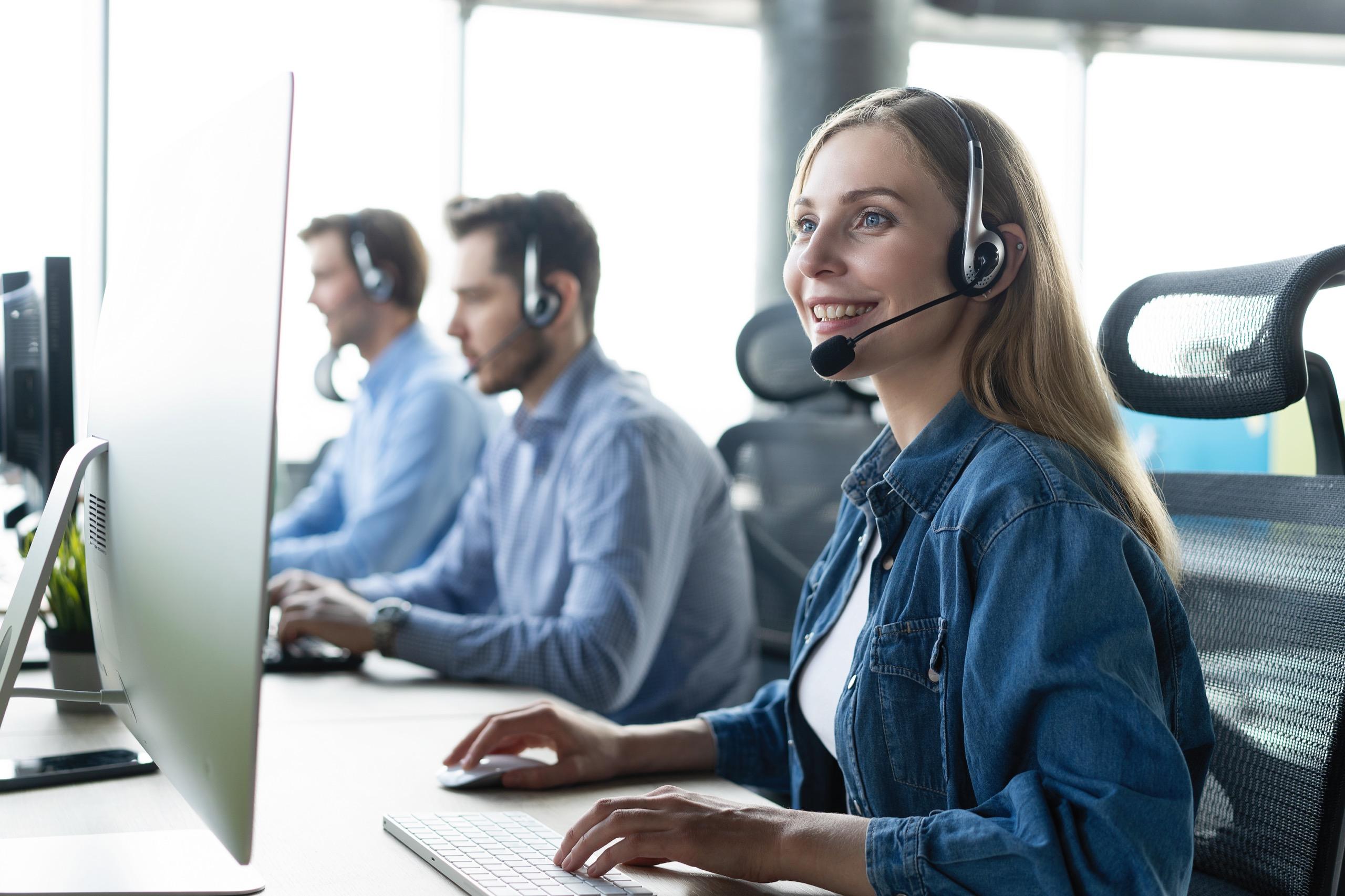 Smiling customer support agent wearing a headset while working on a computer.