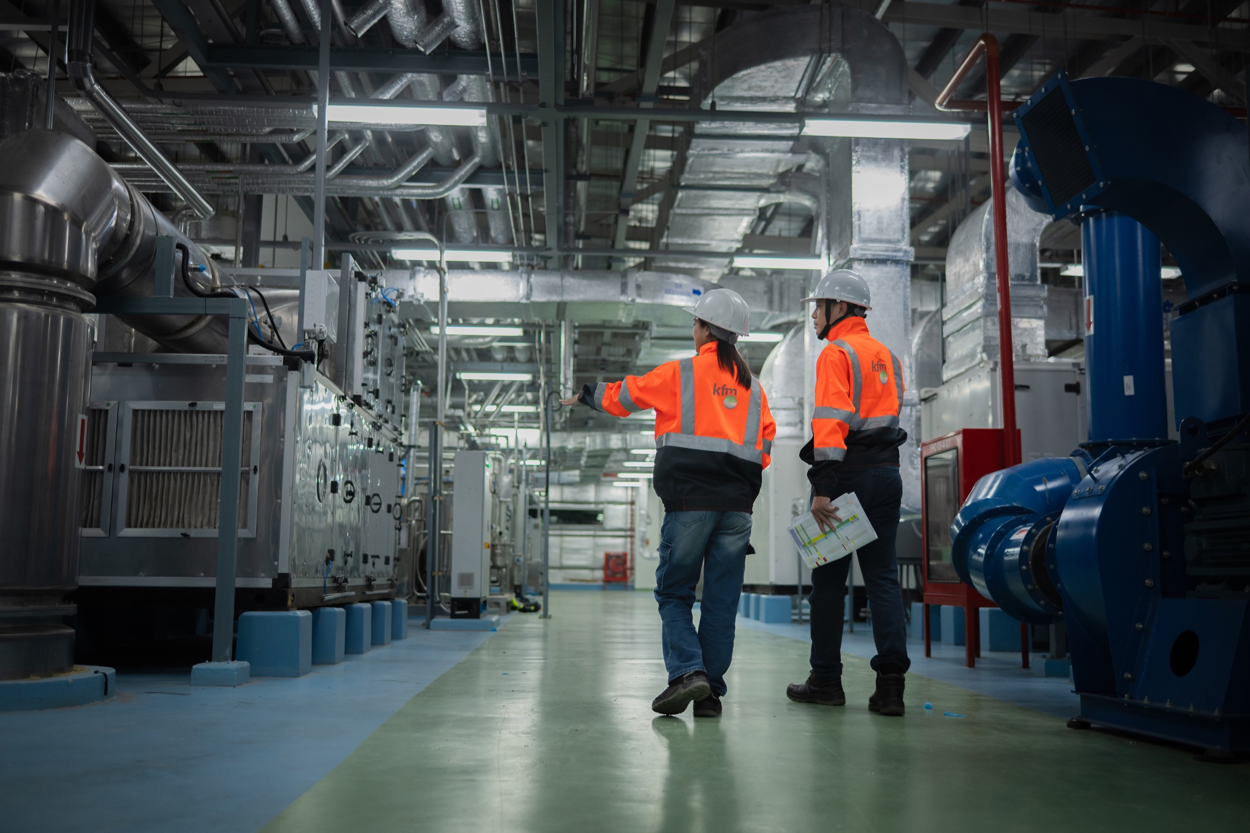 Engineers in safety gear reviewing equipment in a mechanical facility.